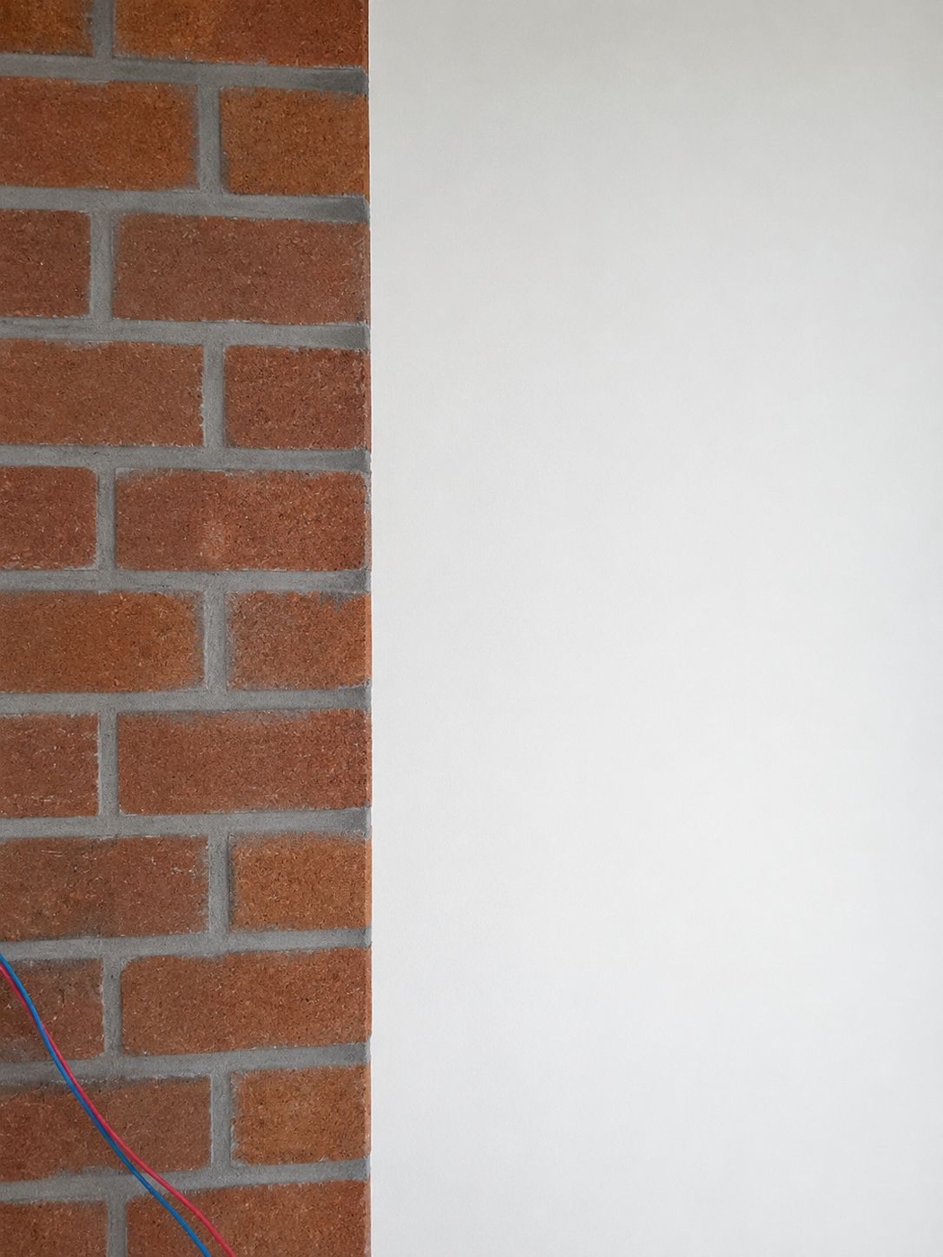An interlock brick wall — exposed natural brick on the left and a smooth plastered, paint-ready finish on the right